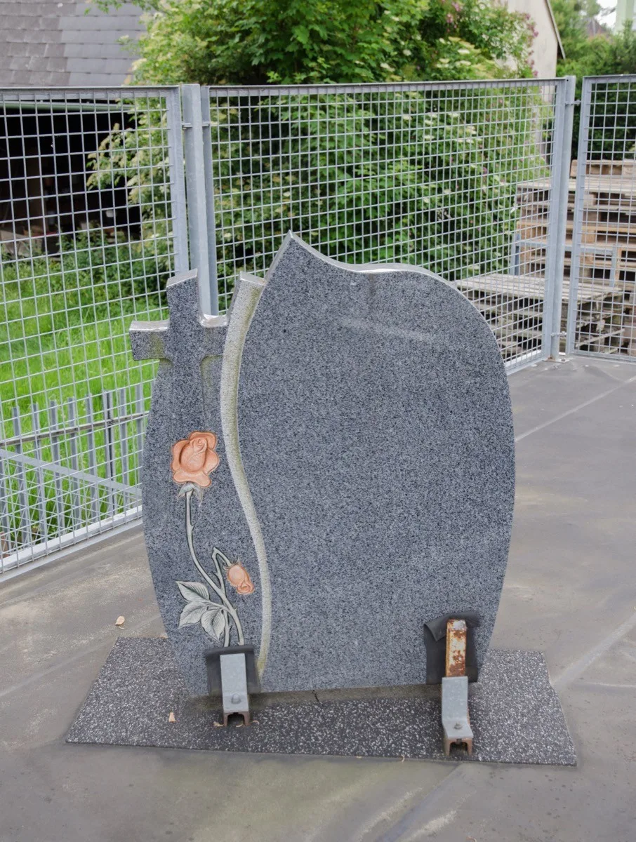 Grauer Grabstein mit Kreuz und farbiger Rose am Rand, ohne Inschrift