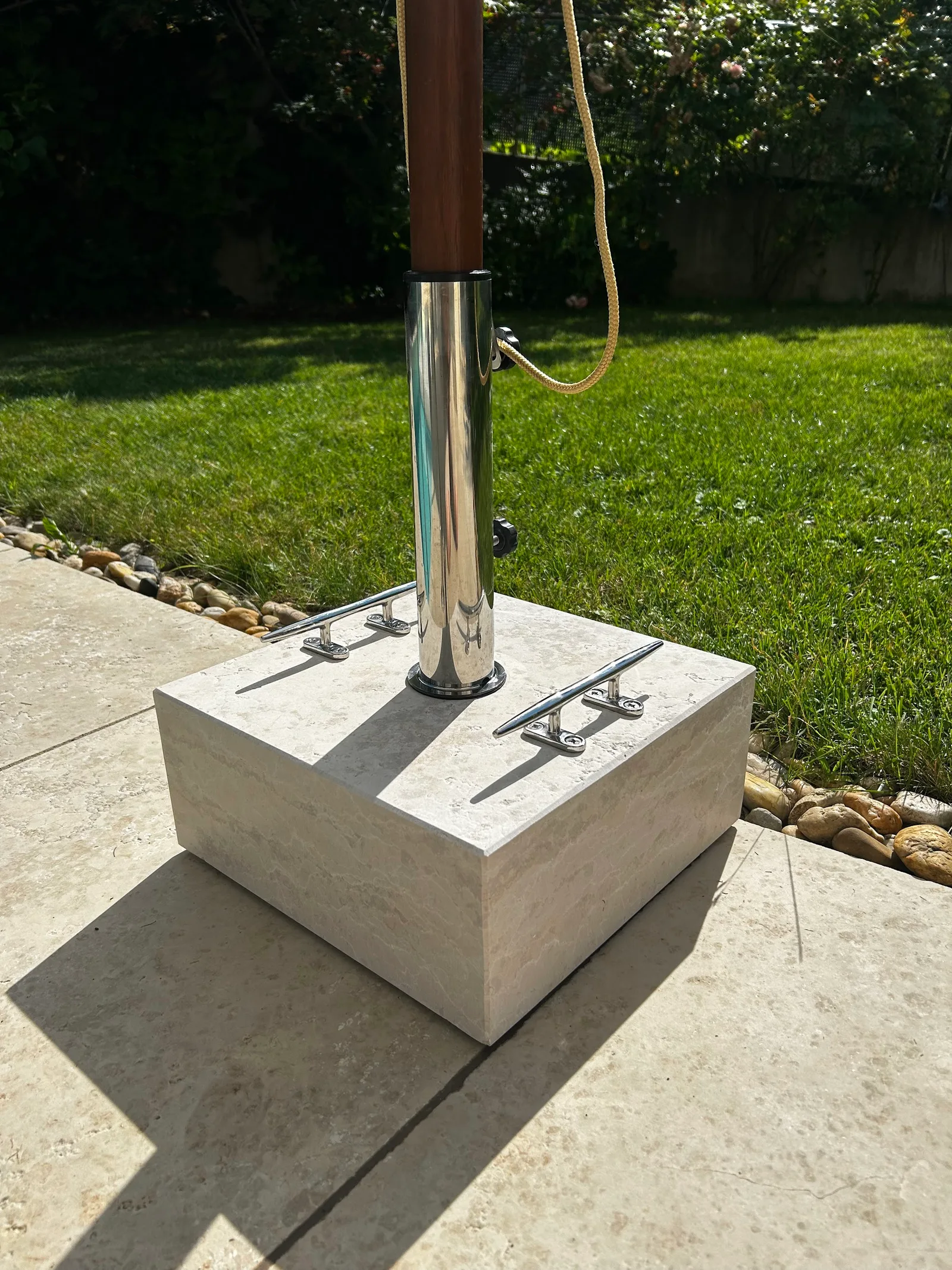 Sonnenschirmständer aus hellem Stein auf einer Terrasse mit gleichen Platten, dahinter Rasen