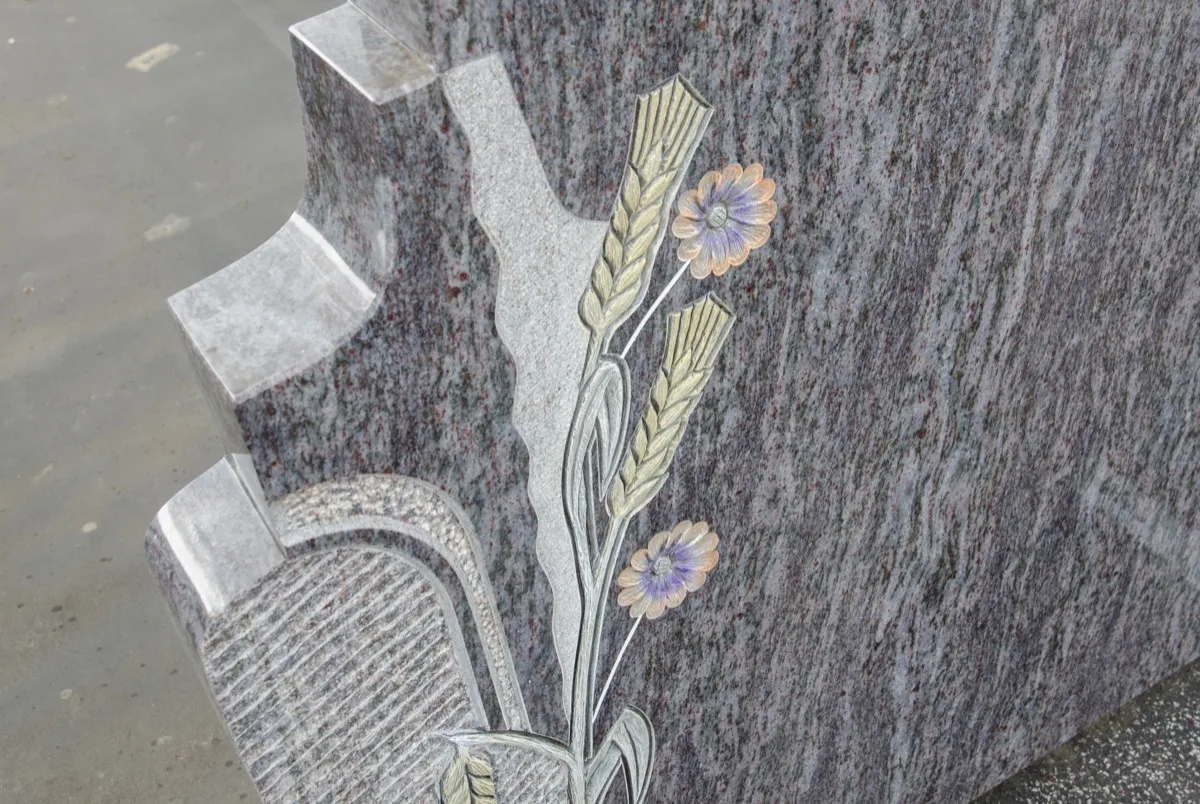 Grabstein mit Ähren und Blumen als Ornament, seitlich ein heller Sockel